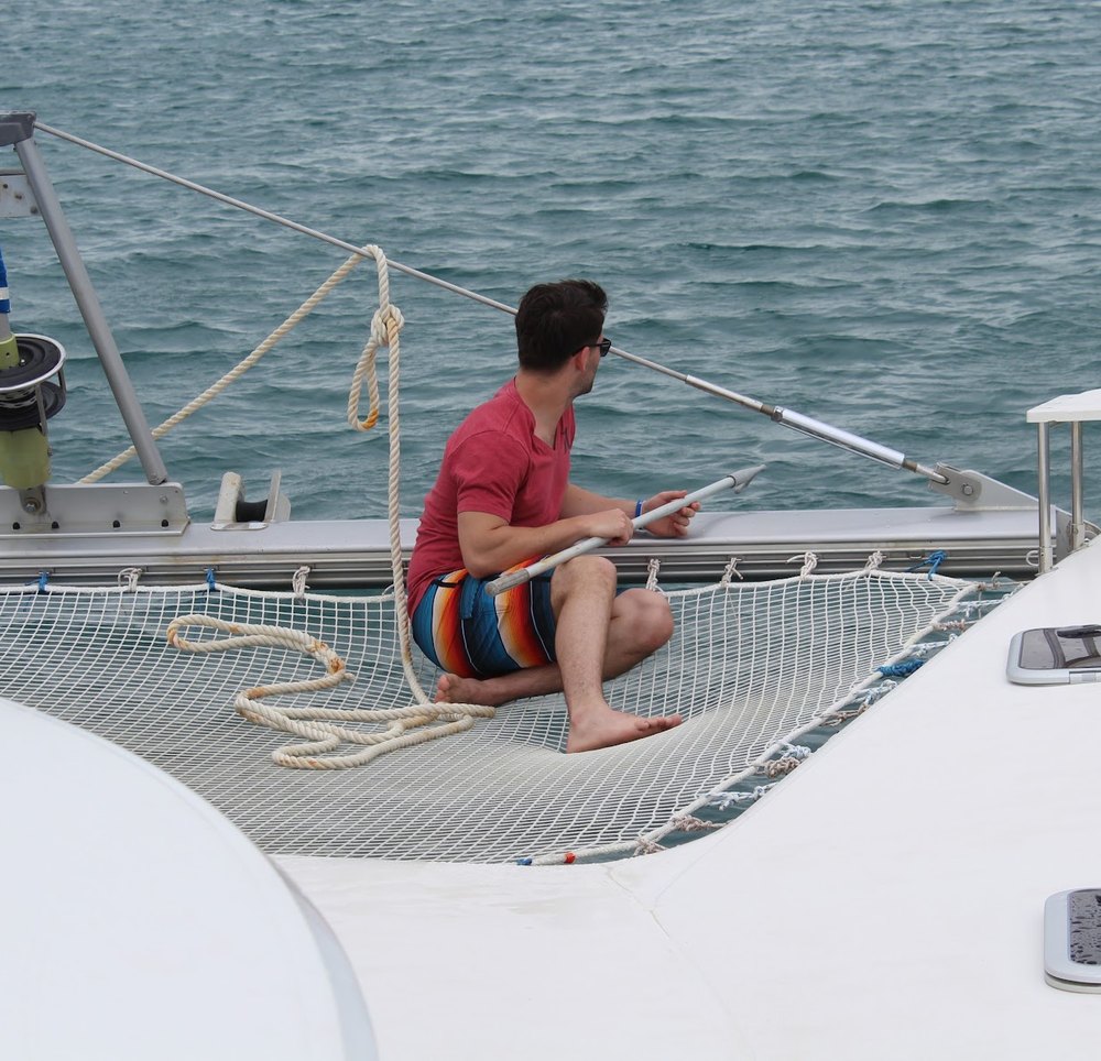 Alex sitting on the net of a sailing catamaran out on the water